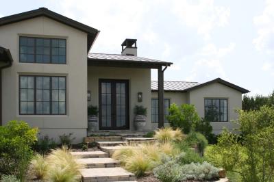 Steel-and-glass entry doors flanked by olive trees in stone urns